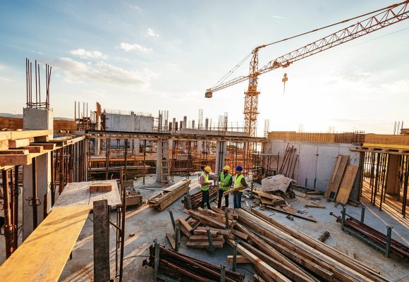 Construction industry concept - architects and engineers discussing work progress between concrete walls, scaffolds and cranes.