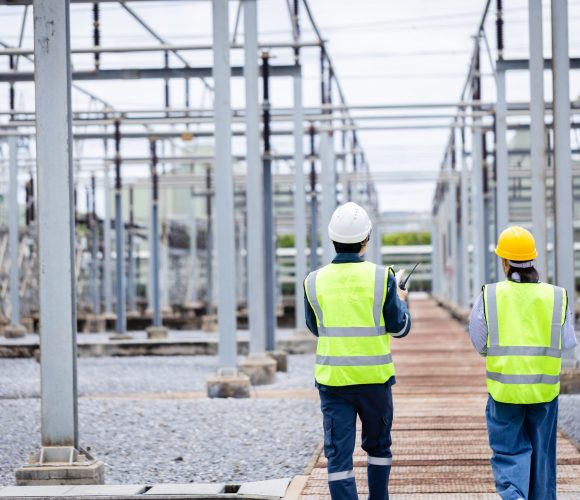 An engineer is working at high voltage power substation performing inspection and check of infrastructure to ensure safety and proper operation of electrical system